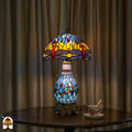 Verlichte Tiffany tafellamp Libellula Azurea ⌀30 op ronde houten tafel voor lichtbeige gordijnen, kap en glas-in-lood voet volledig verlicht, theekopje op schotel naast de lamp