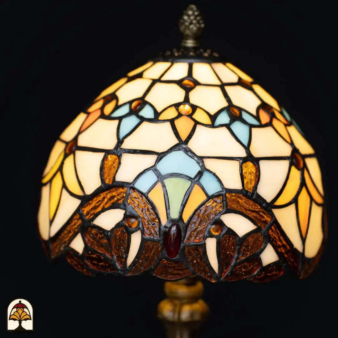 Gros plan abat-jour en dôme allumé lampe de table Tiffany Baroque – verre crème et ambré avec formes d'arches bleu clair et turquoise, cabochon en verre rouge au centre
