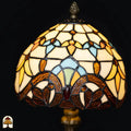 Close-up verlichte koepelkap Tiffany tafellamp Baroque – crème en amber glas met lichtblauwe en turquoise boogvormen, rode edelsteen in center