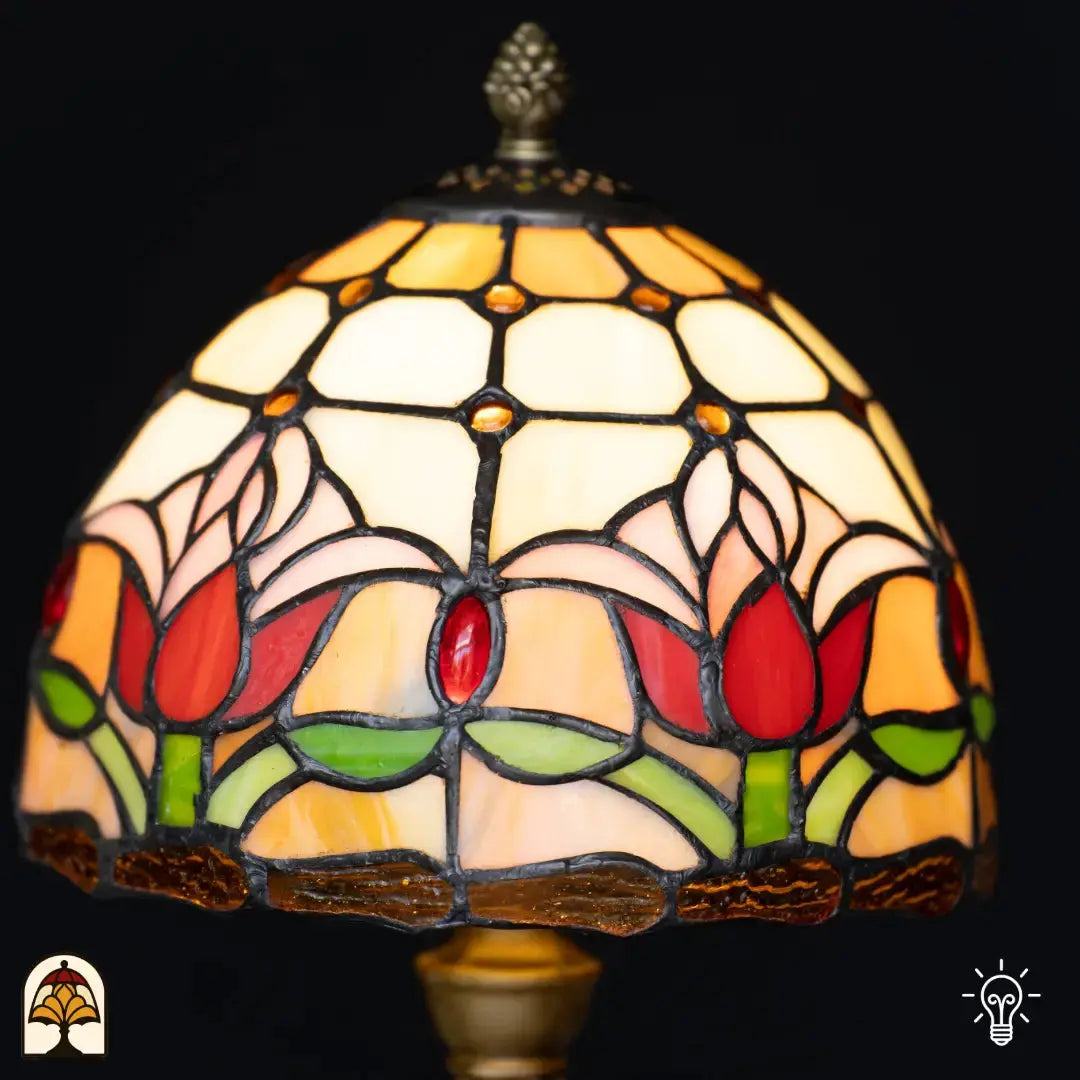 Gros plan abat-jour en dôme allumé lampe de table Tiffany Tulipa – tulipes rouges et roses sur vitrail crème et orange avec cabochons en verre rouges