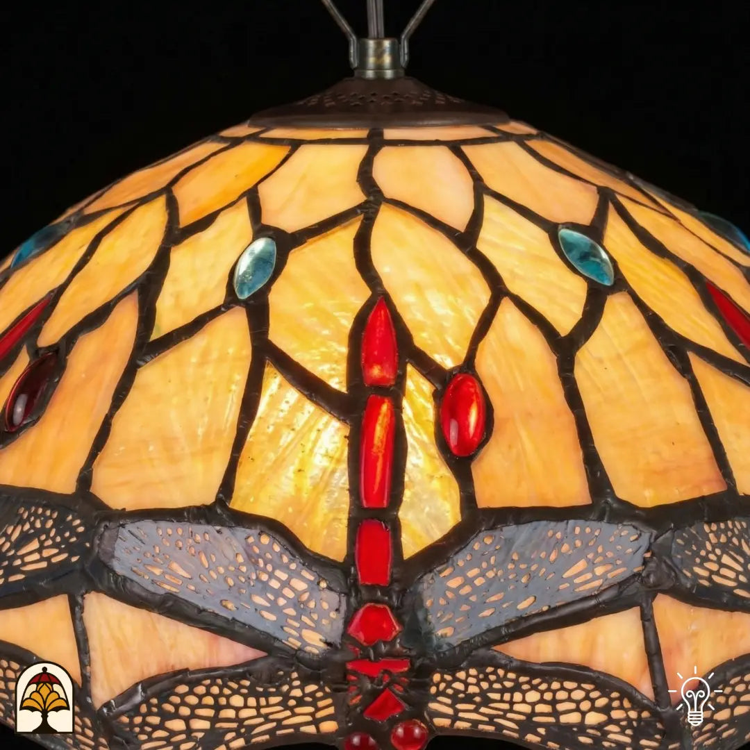 Gros plan abat-jour allumé suspension Tiffany Libelle, vitrail jaune-ambré avec gouttes rouges et accents bleus, motifs de libellules le long du bord