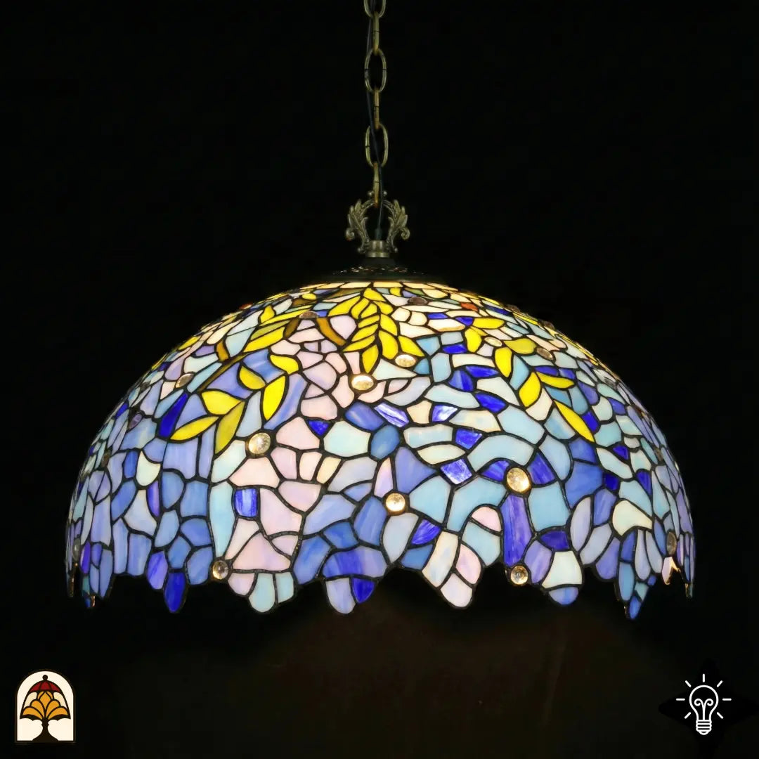 Suspension Tiffany Drizzle Bleu ⌀50 éteinte sur fond sombre, abat-jour dôme à panneaux de vitrail lilas-bleu et turquoise, motifs de feuilles jaunes, accents ronds en cristal, bordure festonnée, chaîne en bronze