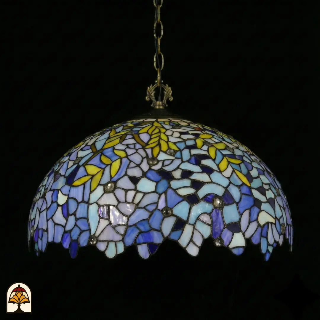 Suspension Tiffany Drizzle Bleu ⌀50 éteinte sur fond sombre, abat-jour dôme lilas-bleu et turquoise avec accents de feuilles jaunes et bord festonné, chaîne en bronze