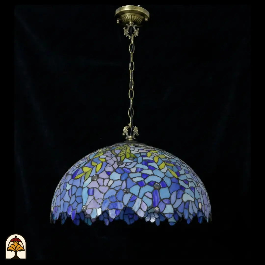 Suspension Tiffany Drizzle Bleu ⌀50 éteinte sur fond sombre, abat-jour dôme bleu et violet avec accents de feuilles jaunes et bordure festonnée, chaîne en bronze avec rosace de plafond