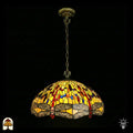 Onverlichte Tiffany hanglamp Libellula Aurelia ⌀50 op donkere achtergrond, grote koepelvormige kap met gele glas-in-lood panelen, libellenfries onderaan, rode en blauwe juwelen, bronzen ketting en plafondrozet