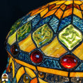 Detailopname van tiffany lamp glas-in-lood bovenzone verlicht, groene diamantvormige glaskralen op ambergeel en blauw getextureerd glas, met roodbruine ronde kralen langs de rand