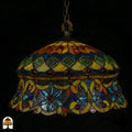 Tiffany lamp hanglamp onverlicht van dichterbij, koepelvormige kap met ambergele bovenzone met groene glaskralen, en blauwe onderzone met lichtblauwe bloemkralen en rode glaskralen op paarsgrijs glas
