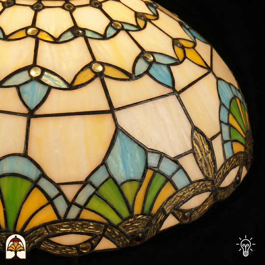 Gros plan du haut de l'abat-jour Barok ⌀40, panneaux de vitrail crème avec formes florales jaunes et bleues, éventail bleu-vert, bordure décorative en bronze en bas