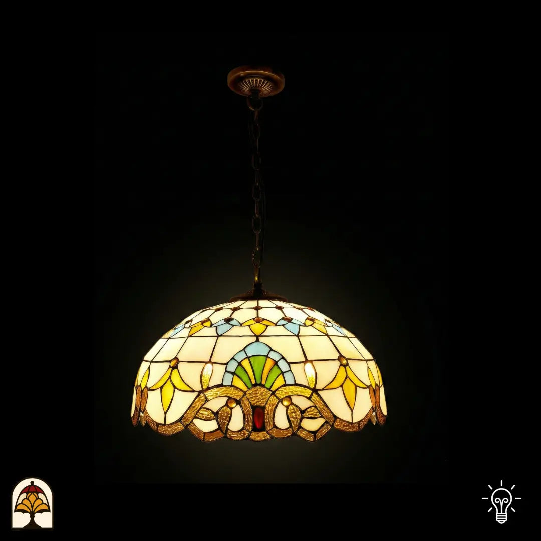Suspension Tiffany Barok ⌀40 allumée sur fond sombre, abat-jour en forme de dôme avec panneaux de vitrail crème, motifs de tulipes jaunes, éventail bleu-vert, bordure baroque à volutes dorées en bas, cabochon en verre rouge au centre, chaîne en bronze et rosace de plafond