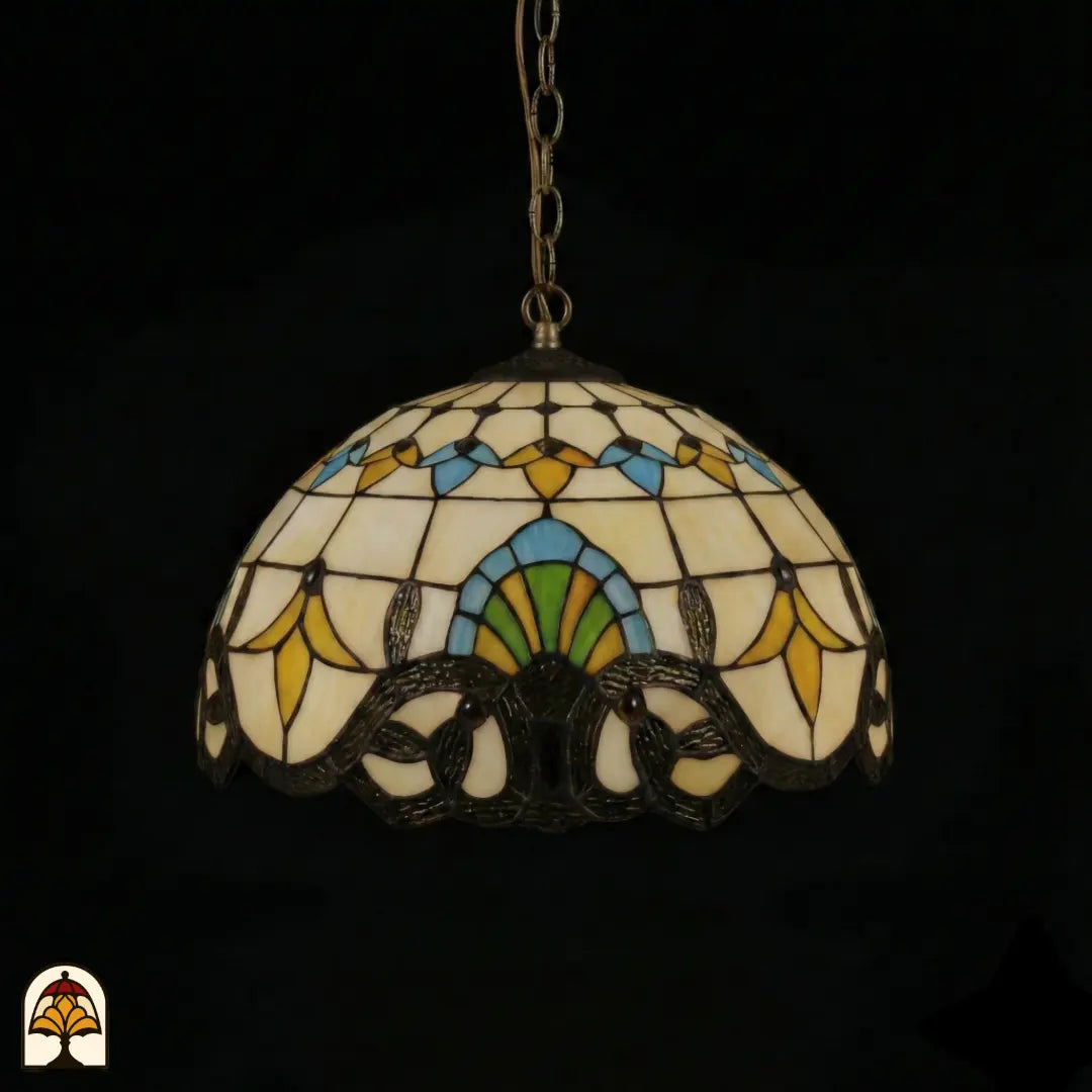 Suspension Tiffany Barok ⌀40 éteinte sur fond sombre, abat-jour à panneaux crème, motifs de tulipes jaunes, accents bleus et verts, bordure baroque sombre à volutes en bas, chaîne en bronze
