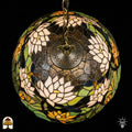 Bovenaanzicht van tiffany lamp hanglamp verlicht, koepel met witte en geel-oranje lotusbloemen en groene waterleliebladen rondom de centrale bronzen ventilatieplaat, donkerblauw glas in het midden