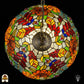 Bovenaanzicht van tiffany lamp hanglamp verlicht, ronde koepel met symmetrisch patroon van oranje en gele rozen, rode glaskralen en groene bladeren, centrale bronzen ventilatieplaat zichtbaar