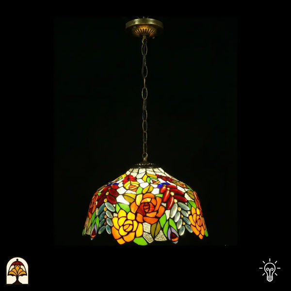 Suspension Tiffany allumée, abat-jour en vitrail en dôme avec roses orange-jaune, cabochons en verre ovales rouges et feuilles vertes sur fond blanc, bord festonné, suspendue à une chaîne en bronze avec rosace de plafond ornée