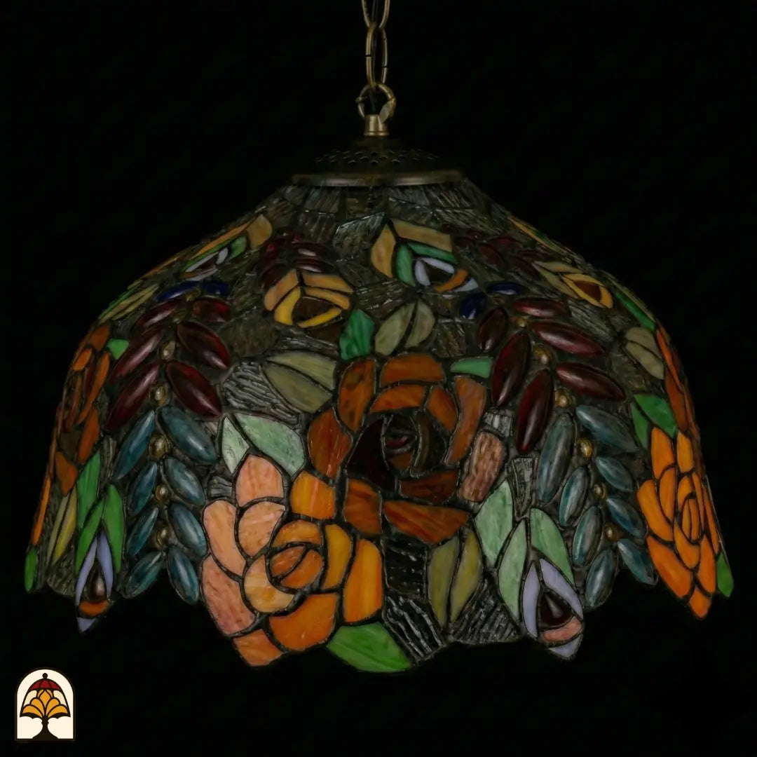 Suspension Tiffany éteinte en gros plan, abat-jour en dôme avec roses orange, brunes et roses, verre texturé vert-gris et feuilles colorées et cabochons en verre ovales