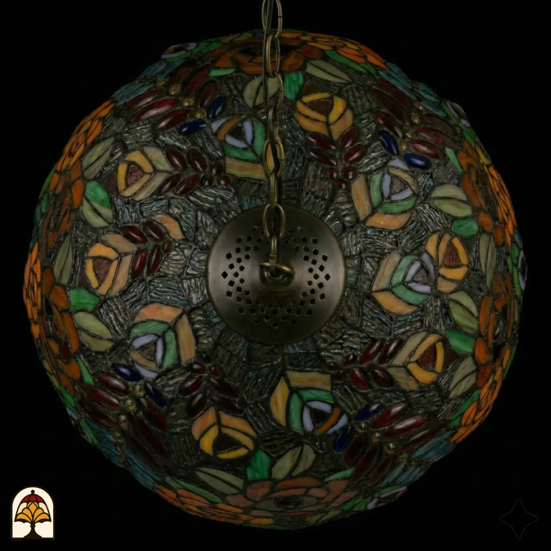 Vue de dessus de suspension lampe Tiffany éteinte, dôme au motif symétrique de roses orange et roses, feuilles colorées et cabochons en verre sur verre texturé gris, plaque d'aération en bronze visible