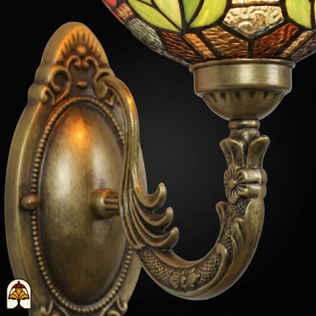 Gros plan de la platine murale en bronze avec plaque ovale en relief et bras courbé, dessus de l'abat-jour en vitrail floral vert et ambré visible