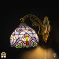 Verlichte Tiffany wandlamp Royal Mosaic met lavendelblauwe glas-in-lood kap, crèmegele bloemmotieven en kleurrijke juwelen op bronzen sierlijke arm