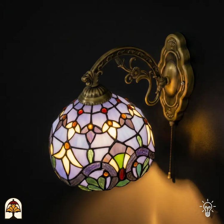 Zijaanzicht verlichte Tiffany wandlamp Royal Mosaic met bolronde lavendelblauwe kap en bronzen arm met druiventros- en bloemmotieven