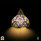 Frontaal aanzicht verlichte Tiffany wandlamp Royal Mosaic, koepelkap in lavendel met crèmegele bloemen en groene bladrand, trekschakelaar zichtbaar
