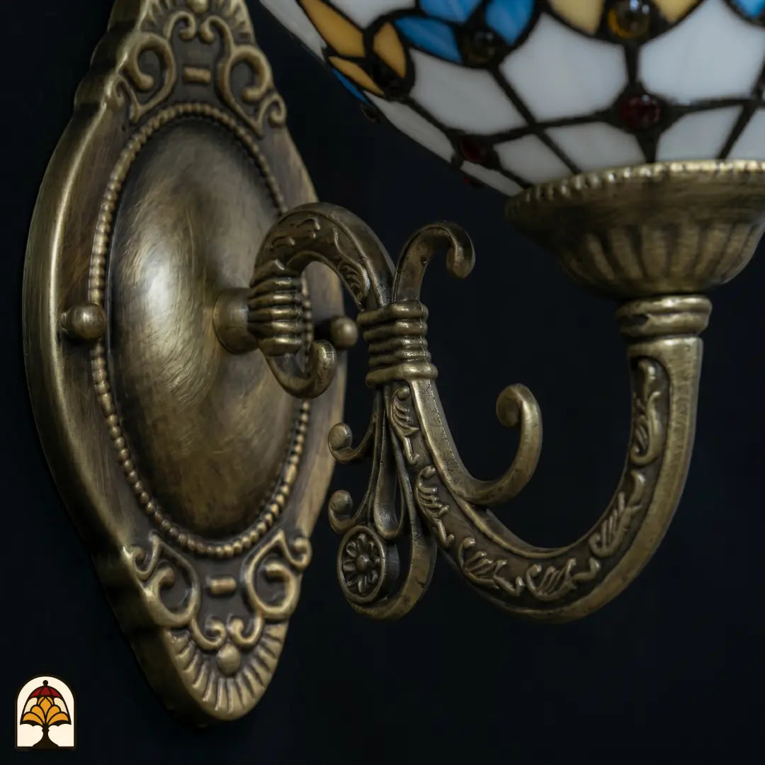 Gros plan de la platine murale en bronze avec plaque ovale en relief et bras courbé, abat-jour en vitrail jaune doré de l'applique murale Tiffany partiellement visible