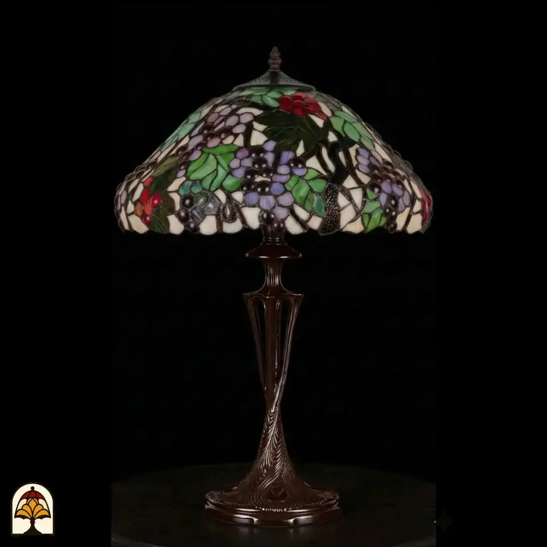 Lampe de table Tiffany Sylva Berria éteinte sur fond sombre, abat-jour avec grappes de raisins lilas et rouges et feuilles vertes, pied vase Art nouveau élancé en bronze