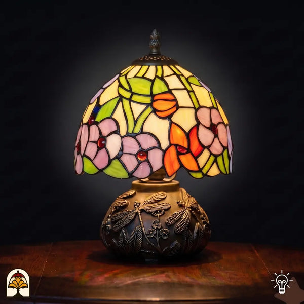 Lampe de table Tiffany Amber Flora Classic ⌀20 cm allumée sur fond noir – abat-jour à motifs de fleurs roses en vitrail, pied libellule en bronze