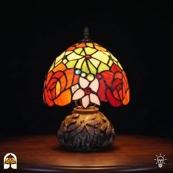 Lampe de table Tiffany Viola Ember ⌀20 cm allumée – abat-jour sphérique avec roses orange-rouge, feuilles vertes sur pied à libellules