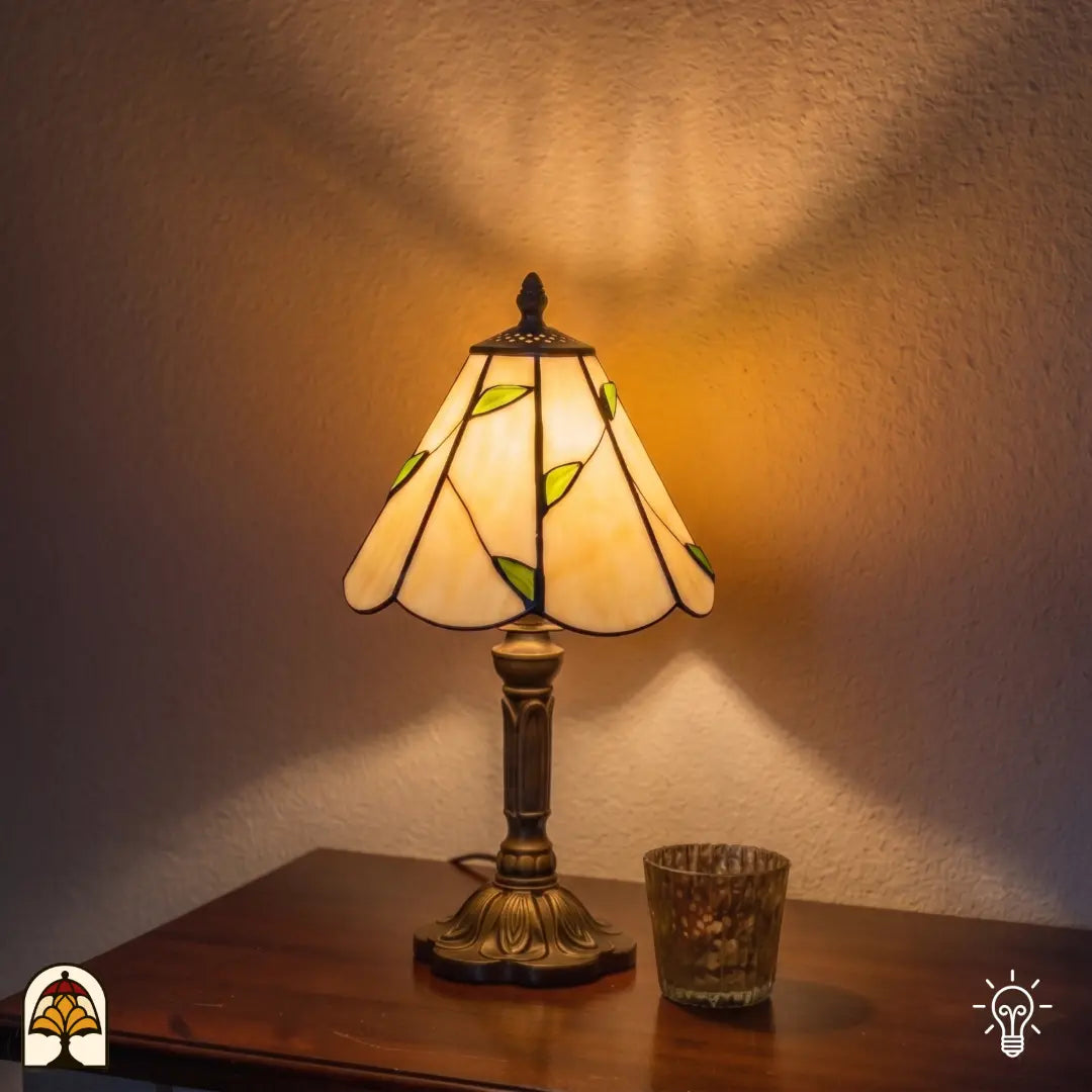 Lampe de table Tiffany Lumina Foliage ⌀20 cm allumée dans un intérieur chaleureux – abat-jour conique blanc crème avec guirlande de feuilles vertes, pied en bronze, lumière chaude
