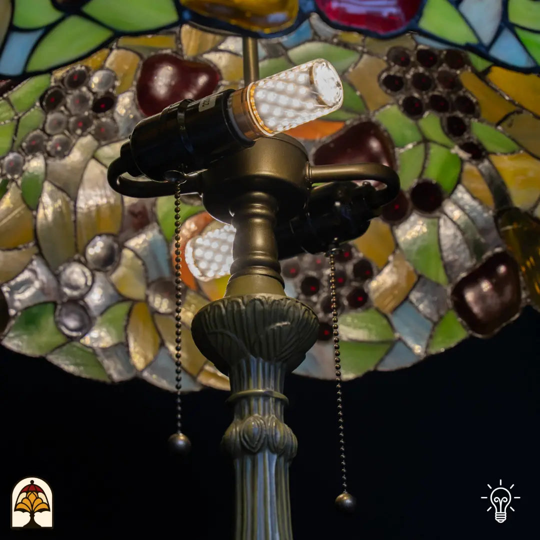 Gros plan douille lampe de table Tiffany Frutta Viva — ampoule LED dans douille en bronze, interrupteurs à chaînette, verre à motif de fruits en arrière-plan