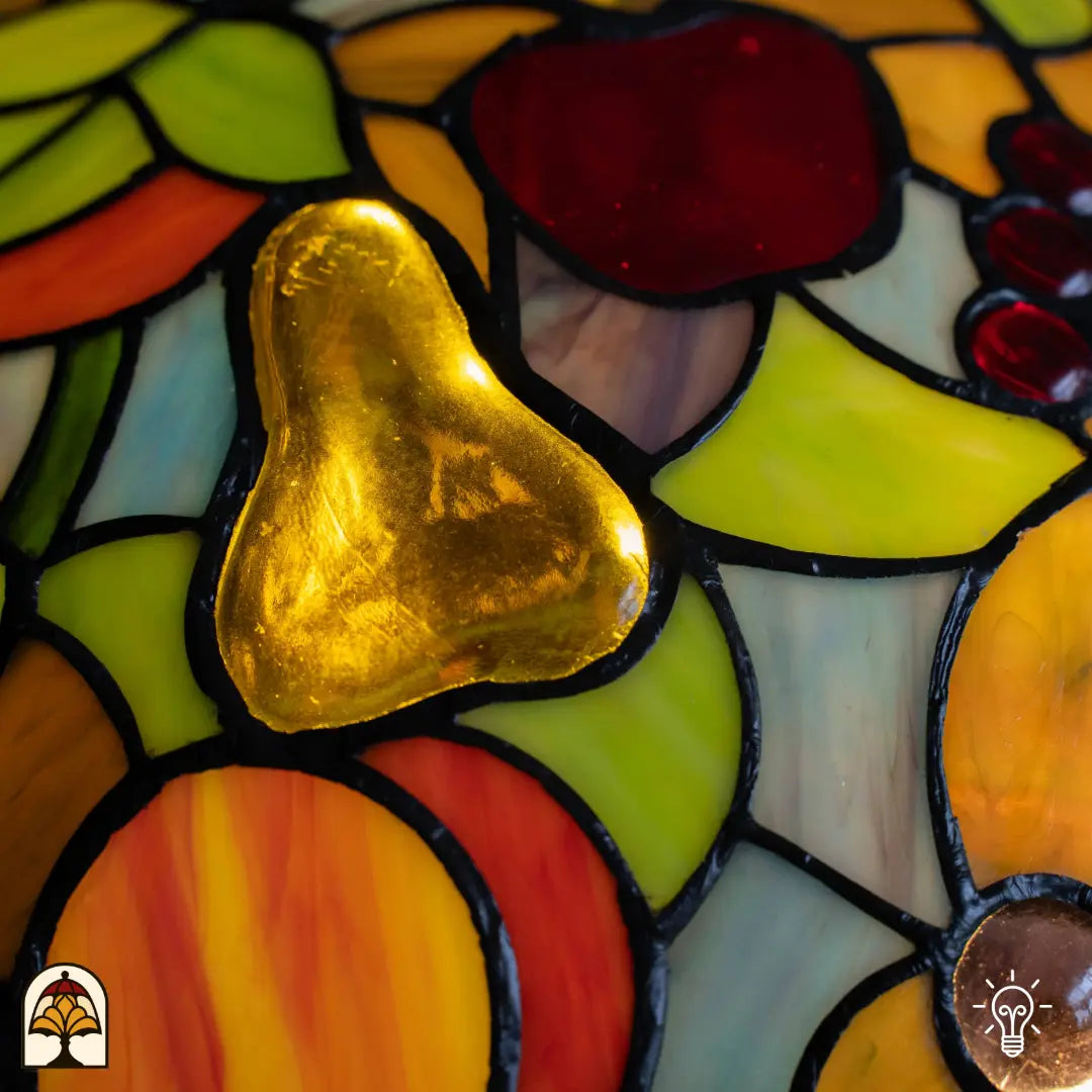 Détail abat-jour lampe de table Tiffany Frutta Viva — poire dorée en verre au centre, pomme rouge et raisins violets tout autour, feuilles vertes