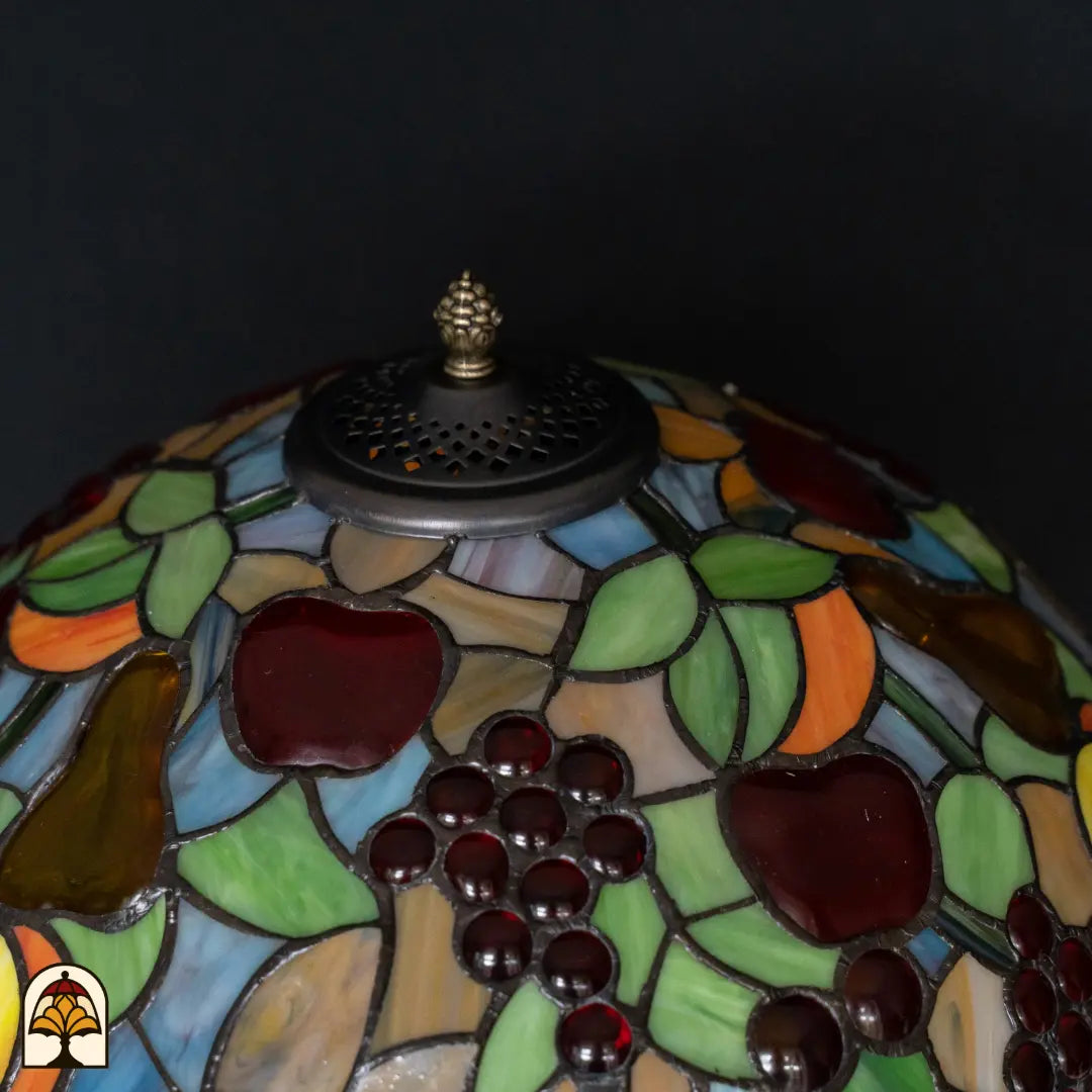 Gros plan du haut de l'abat-jour lampe de table Tiffany Frutta Viva — grille d'aération perforée, motif de fruits avec pommes rouges et raisins tout autour, feuilles vertes