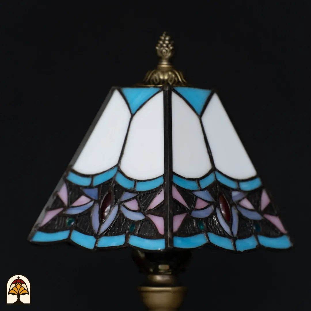 Gros plan abat-jour Tiffany éteint — panneaux supérieurs blancs, bordure bleue, fleurs de lotus violettes et roses, cabochons rouges, verre foncé texturé