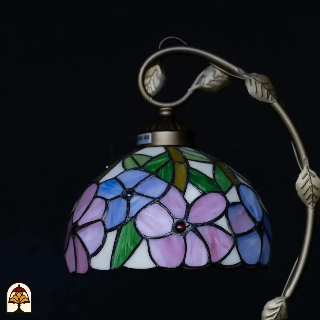 Gros plan abat-jour Tiffany éteint — fleurs bleu/violet et roses sur fond blanc, feuilles vertes, petits cabochons rouges