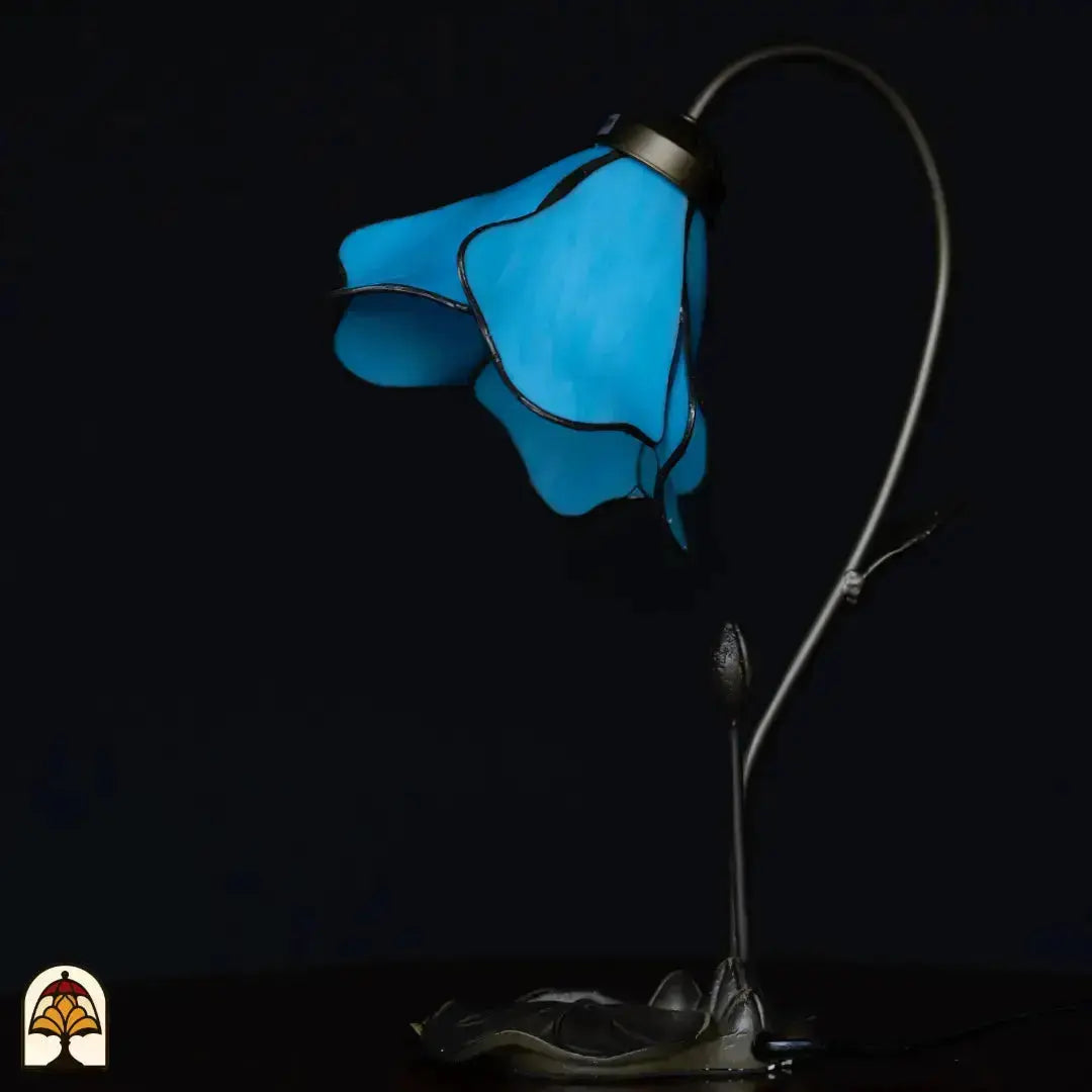 Lampe de table Tiffany éteinte sur fond sombre — abat-jour en fleur de lotus bleue, bras en forme de tige courbée avec bouton, base en feuille de lotus en bronze