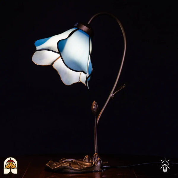 Lampe de table Tiffany allumée avec abat-jour fleur de lotus bleu/blanc, bras courbé en forme de tige avec bouton, base en bronze en feuille de lotus, fond noir
