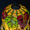 Close-up bovenkant Tiffany kap — geperforeerd ventilatierooster, gele/amber glas met groene bladvormige elementen rondom