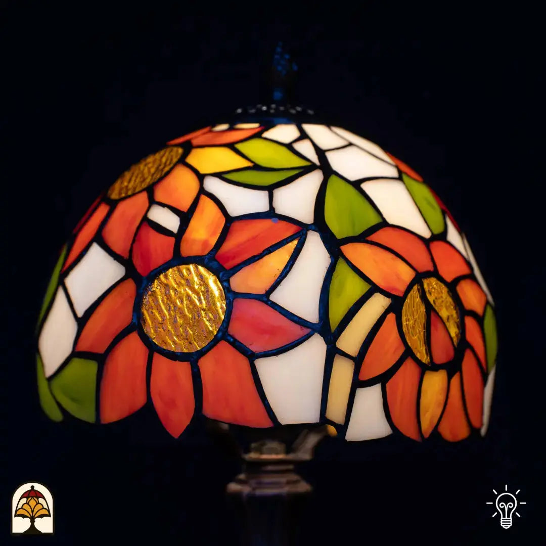 Gros plan abat-jour allumé lampe de table Tiffany Solea — pétales de tournesol orange à coeurs dorés/bruns, feuilles vertes, aplats crème/blancs