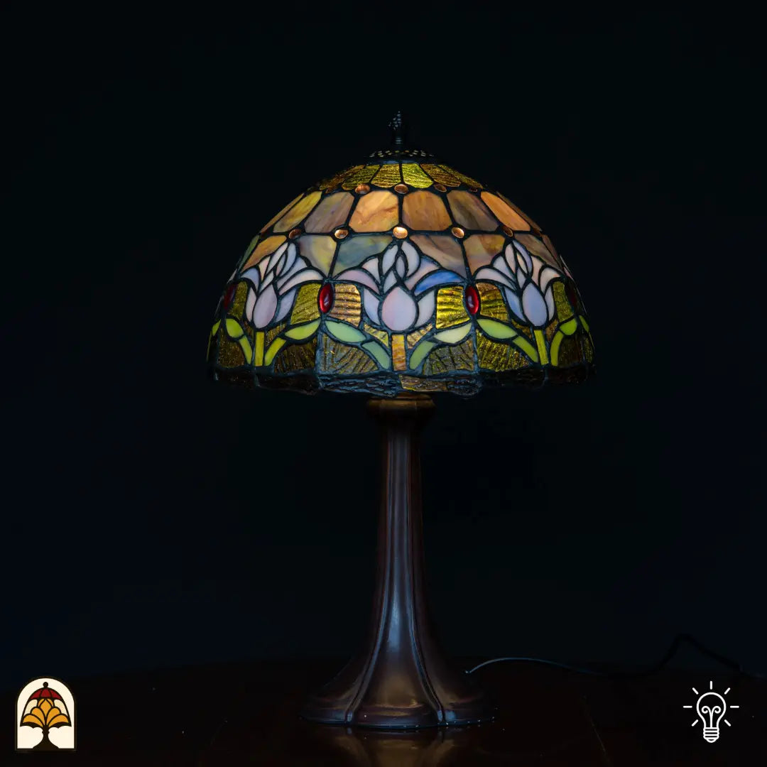 Lampe de table Tiffany Tulipa Lilac Sereno ⌀30 cm allumée sur fond noir – abat-jour en dôme avec tulipes lilas, pied colonne en bronze
