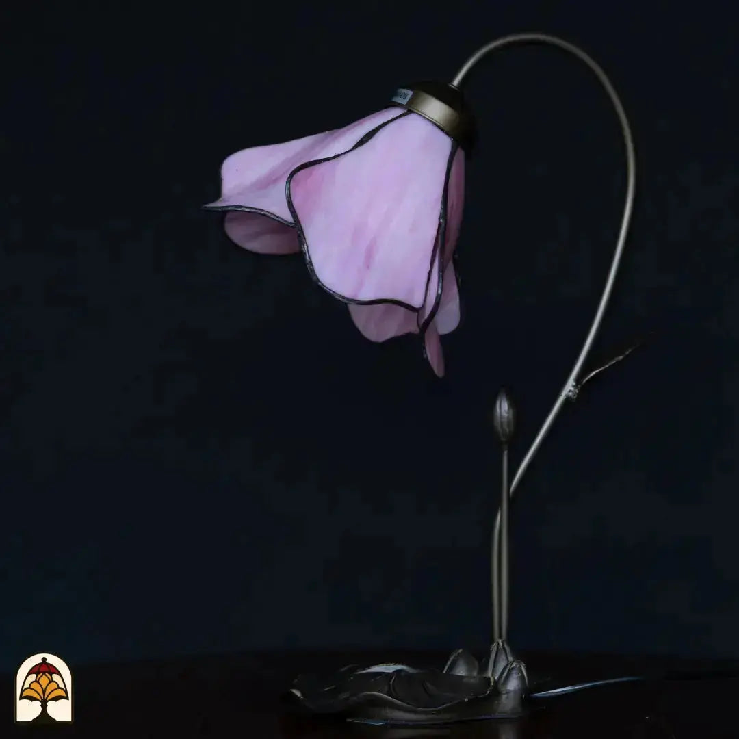 Lampe de table Tiffany éteinte sur fond bleu foncé — abat-jour en fleur de lotus rose, bras en forme de tige courbée avec bouton, base en feuille de lotus en bronze
