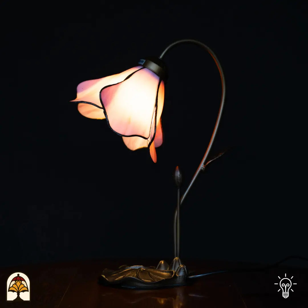 Lampe de table Tiffany allumée avec abat-jour fleur de lotus rose, bras courbé en forme de tige avec bouton, base en bronze en feuille de lotus, fond noir