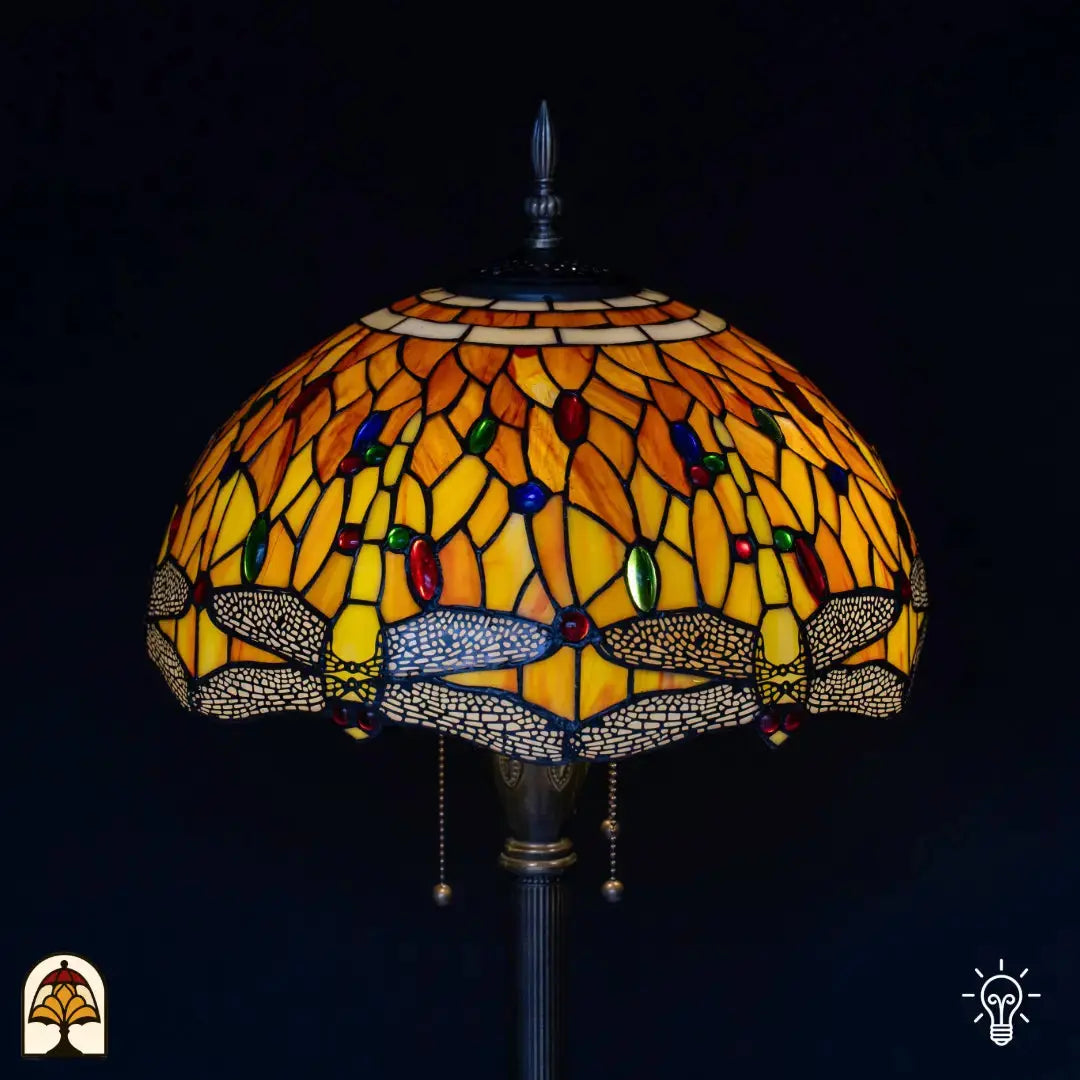 Gros plan abat-jour allumé lampadaire Tiffany Libellula Aurea — verre ambré/jaune/orange avec motif de libellules dans une bordure grise, cabochons en verre rouges et verts, interrupteurs à chaînette
