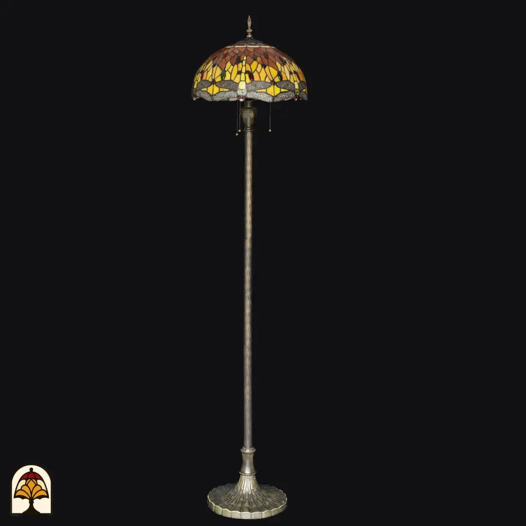 Lampadaire Tiffany Libellula Aurea éteint sur fond noir — abat-jour ambré/jaune/brun avec bordure à libellules, long fût avec base large