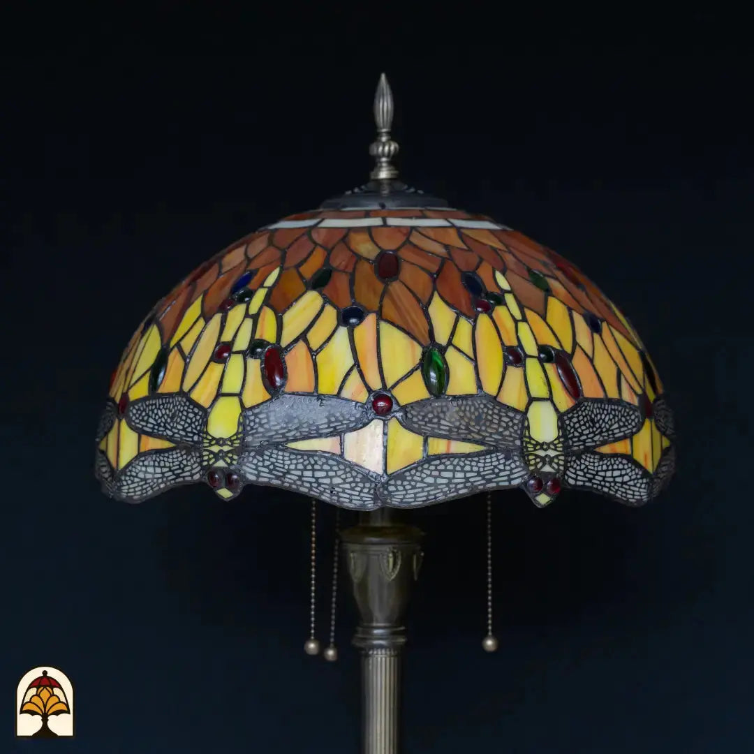 Gros plan abat-jour lampadaire Tiffany Libellula Aurea éteint — verre jaune/orange/ambré avec pierres précieuses rouges, bleues et vertes, bordure de libellules grise en bas